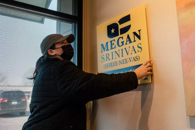 A woman sticks a Megan Srinivas for Iowa House sign to a wall