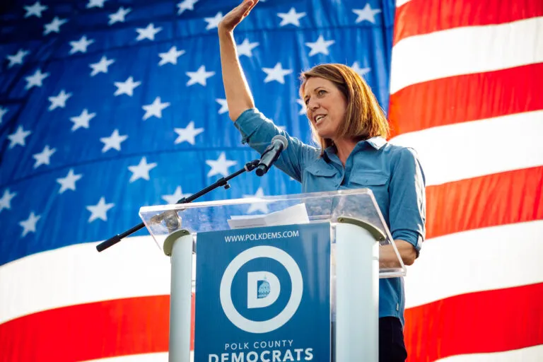 Rep. Cindy Axne waves as she takes the stage in front of a massive American flag.